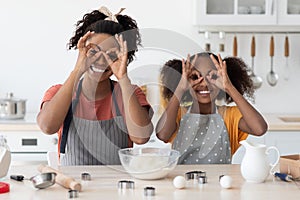 Black mother showing her teen daughter how to make cookies