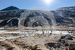 Black mountain witn snow and below with tourists on the ground with brown grass, snow and frozen pond in winter at Zero Point.