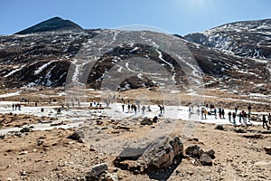 Black mountain witn snow and below with tourists on the ground with brown grass, snow and frozen pond in winter at Zero Point.