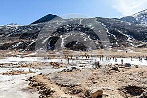 Black mountain witn snow and below with tourists on the ground with brown grass, snow and frozen pond in winter at Zero Point.