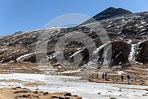 Black mountain witn snow and below with tourists on the ground with brown grass, snow and frozen pond in winter at Zero Point.