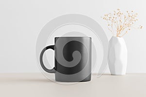 Black mug mockup with a gypsophila in a vase on a beige table