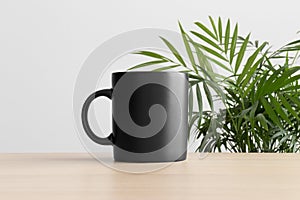 Black mug mockup on the wooden table with a palm plant