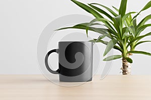 Black mug mockup on the wooden table with a yucca plant