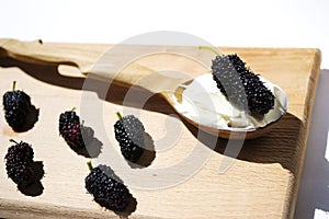 Black mulberry, spoon with sour cream on breadboard,