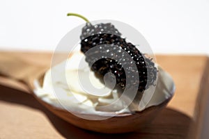 Black mulberry, spoon with sour cream on breadboard, closeup