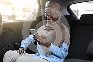 Black muslim business lady in hijab using smartphone while traveling by car