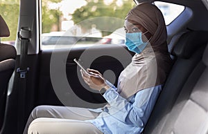 Black muslim businesswoman wearing face mask while using taxi during coronavirus pandemic