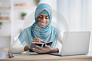 Black Muslim Lady Taking Notes To Notepad While Working At Home Office