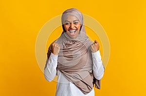 Black muslim woman in headscarf rejoicing success with raised fists