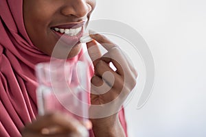 Black Muslim Woman In Hijab Holding Glass Of Water And Taking Pill