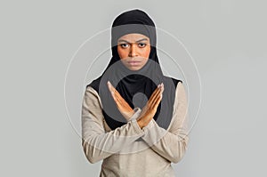 Black muslim woman making denial gesture, keeps arms crossed, rejecting something