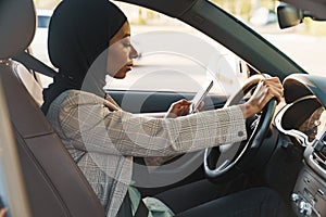 Black muslim woman using cellphone while driving car