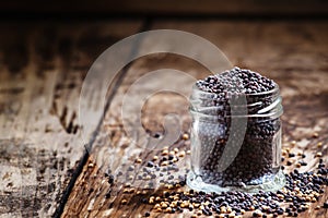 Black mustard seeds in a glass jar on the old wooden background, selective focus