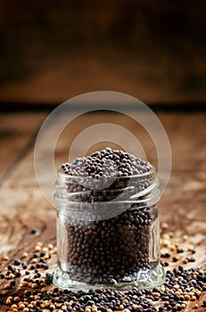 Black mustard seeds in a glass jar on the old wooden background, selective focus