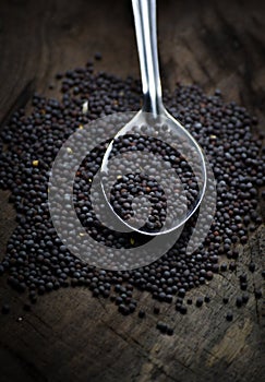 Black mustard seeds on a wooden table.