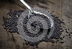 Black mustard seeds on a wooden table.