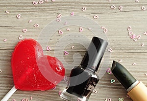 Black nail polish and lipstick displayed with a red heart shape lollipop