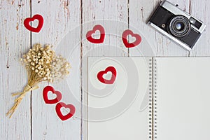 Black notebook with flowers, red heart and camera on wooden table.