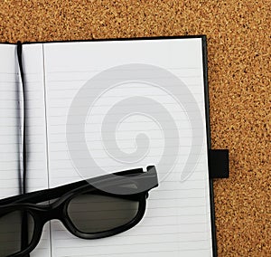 black notebook and glasses on the cork board background.