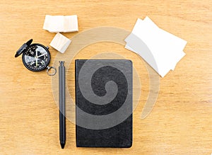 Black notebook, pen, compass and business card on wood table, Mock