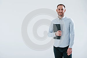 Black notepad in hands. Man in official clothes stands against white background in the studio