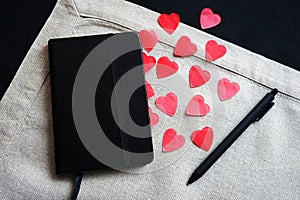 Black notepad next to red hearts on a linen napkin