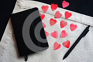 Black notepad next to red hearts on a linen napkin