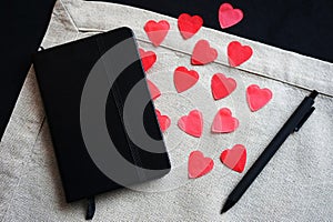 Black notepad next to red hearts on a linen napkin