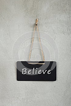 Black notice board, blackboard, chalkboard with text Believe on grey cement wall