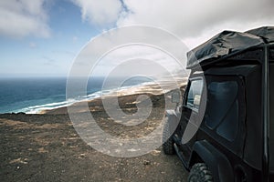 Black off road car parked on the top of a valley with amazing view on a wild beach with nobody - off grid roof tent and adventure