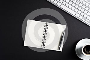 Black office desk table with blank paper notepad, pen, pc keyboard, cup of coffee. Top view with copy space, flat lay. Elegant