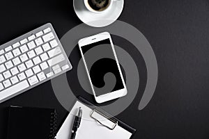 Black office desk table top view. Flat lay smartphone with blank screen mockup, pc keyboard, cup of coffee, clipboard, pen,