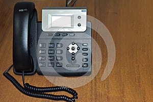 Black office IP phone on a wooden table. The concept of a modern office, internal communication.