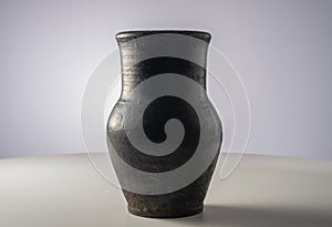 Black old jug. Handmade jar from clay standing on white table isolated on gray background in studio. Earthenware for