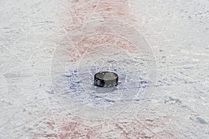 Black old puck lies in center of throw-in circle on skate-cut ice of hockey rink.