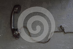 Black old telephone receiver hanging on black background with texting space, waiting for phone call, vintage telephone