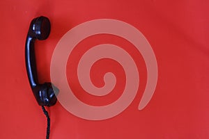 Black old telephone receiver hanging on red background with texting space, waiting for phone call,