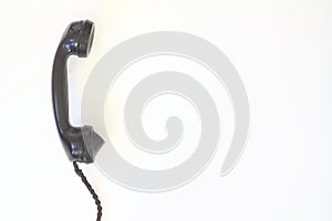 Black old telephone receiver hanging on white background with texting space, waiting for phone call, vintage telephone
