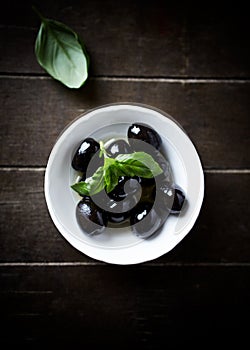 Black olives with fresh basil on rustic wooden background. Soft focus. Close up.