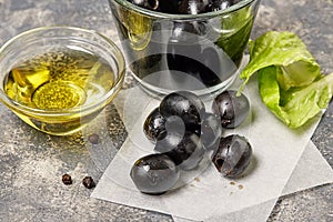 Black olives, glass bowl with oil on background.