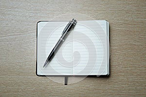 Black opened notebook and pen on the table on left top view.