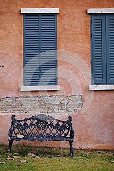 Black ornated outdoor bench on the green grass with orange rustic wall background