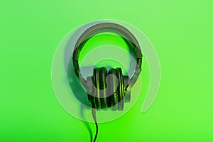 Black overhead headphones neon background, copy space. Modern technology flat lay with over-ear earphones and cable, modern
