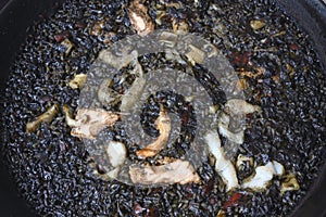 Black paella with cuttlefish ink and seafood in a black pan in a Spanish restaurant. A traditional dish of Spanish cuisine.