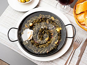 Black paella with cuttlefish ink and seafood in black pan in Spanish restaurant. Traditional dish of Spanish cuisine