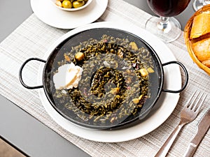 Black paella with cuttlefish ink and seafood in black pan in Spanish restaurant. Traditional dish of Spanish cuisine