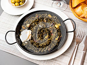 Black paella with cuttlefish ink and seafood in black pan in Spanish restaurant. Traditional dish of Spanish cuisine