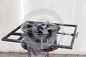 A black painted aluminum alloy wheel is mounted on a special frame during drying in a chamber in a vehicle body repair workshop.