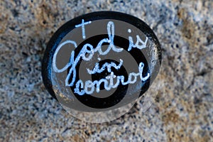 Black painted rock with message stating God is in control